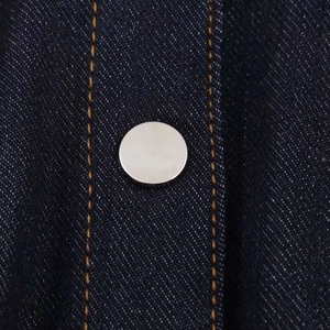 Vue macro extrême du bouton argenté et des coutures jaunes sur le tissu denim bleu foncé