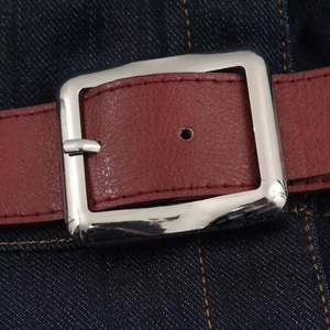 Détail d'une ceinture en cuir bordeaux avec boucle argentée sur robe en jean