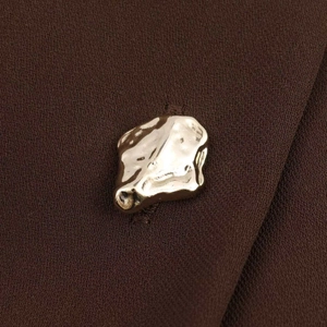Detail of elegant gold irregular textured metal button on a dark brown fashion dress