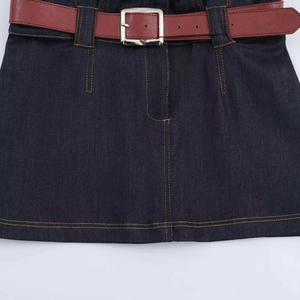Détail de la robe en jean bleu foncé avec coutures contrastées et ceinture en similicuir brun