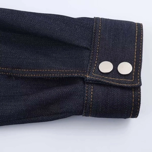 Détail du poignet d'une robe en jean bleu foncé avec boutons argentés et coutures orange