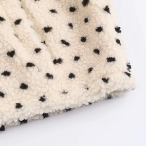 Close-up detail of soft cream fleece fabric with black polka dots and fluffy texture