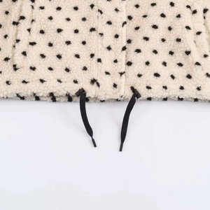 Detailed close-up of cream fleece jacket fabric with black polka dots and hem drawstring