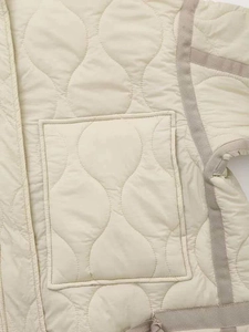 Detailed view of beige quilted jacket featuring onion patterns and grey contrast trimming
