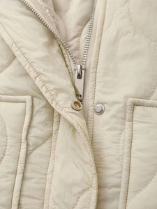 Detailed view of beige quilted jacket with silver metal zipper and snap buttons closure