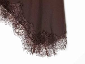 Close-up of asymmetrical eyelash lace trim on a dark brown satin skirt hemline