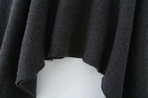 Detail of soft charcoal grey knitted poncho fabric showcasing hem texture and drape