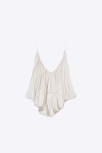 Detailed view of the gathered pleats and glossy satin fabric on the cream camisole top