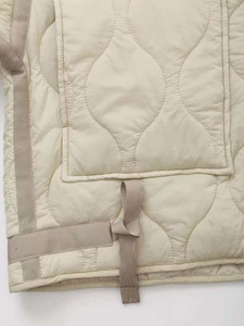 Detail view of cream white wave-quilted jacket featuring large pocket and nylon texture