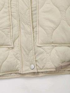 Detailed view of beige quilted jacket with wave patterns and silver metal snap button