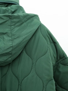 Detail of dark green quilted jacket featuring a hood and zipper on the neckline