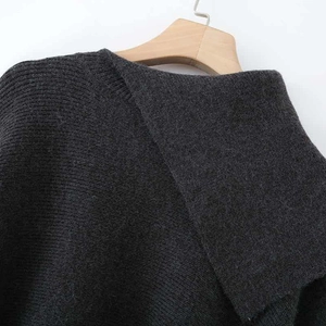 Dark grey chunky knit sweater with asymmetric collar and ribbed texture on wooden hanger