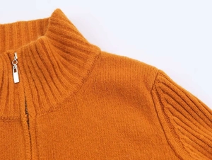 Detail of orange ribbed knit collar with silver half-zipper on a stylish sweater