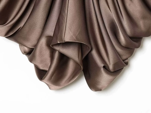 Detailed macro view of high-quality brown satin fabric with soft drapes and pleated texture