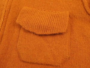 Close-up of bright orange knit sweater showing rib-knit pocket detail and fuzzy texture