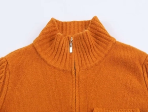 Detail of caramel knit sweater featuring a ribbed high neck and metal half-zip closure