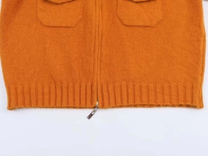 Detailed view of orange knit cardigan featuring dual pockets and metal zipper closure