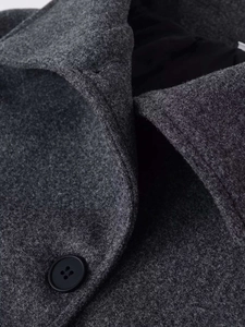 Détail de couture du manteau en laine gris foncé montrant le revers et un bouton noir élégant