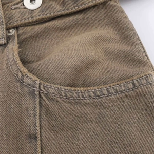 Detail of high waist khaki denim jeans featuring metal button and rivet with washed texture
