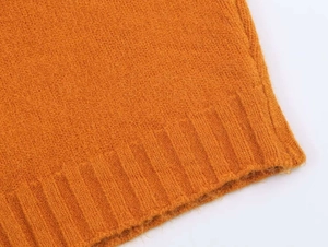 Detailed macro view of orange knit sweater showing ribbed hem texture and soft wool fabric