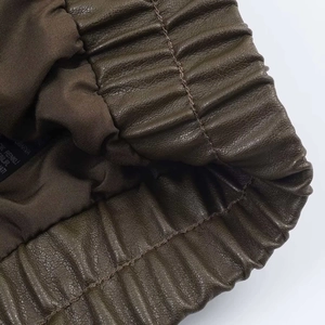 Detail of gathered elastic hem and olive brown faux leather texture on a jacket