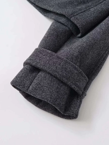 Détail du poignet d'un manteau en laine gris foncé montrant la texture du tissu et la bride