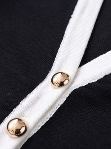 Detalle de vestido de punto negro con ribete blanco y botones dorados decorativos