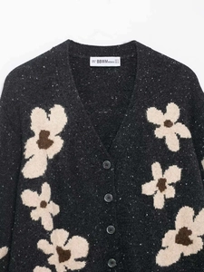 Macro shot of dark grey floral knit cardigan fabric and brand neck label detail
