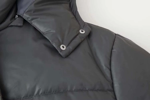 Detail of black quilted jacket featuring silver metal snap buttons and fine stitching