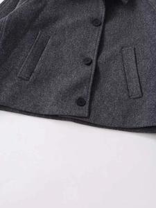 Détail d'une veste en laine gris foncé avec trois boutons noirs et des poches verticales