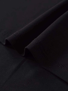 Close-up of high-quality black knit fabric showing the asymmetrical hem stitching details