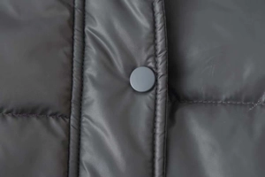 Macro shot of dark quilted winter jacket featuring matte snap button and fine stitching