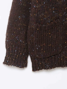 Détail d'un cardigan en grosse maille marron foncé avec mouchetures et poignets côtelés