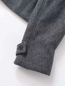 Détail du poignet en laine gris foncé avec bouton noir et couture fine de la veste