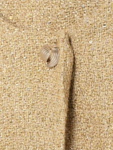 Gros plan sur le tissu en tweed doré avec fils métalliques et bouton spirale doré