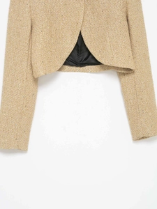 Détail de la fente arrière d'une veste en tweed avec texture dorée et doublure