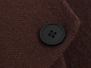 Détail d'un bouton noir classique sur un gilet en maille texturée marron foncé