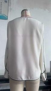 Detail view of contrast black piping on the back of a cream long sleeve chiffon blouse