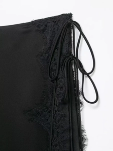 Detail of silk-satin black skirt featuring delicate eyelash lace trim and side drawstring ties