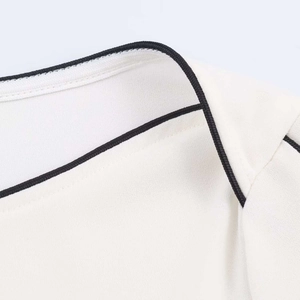 Close-up detail of off-white chiffon blouse featuring elegant black piping on the neckline