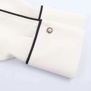 Off-white chiffon blouse cuff detail with black contrast piping and pearl accent button