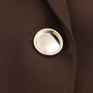 Detailed close-up of a glossy gold metal button on deep brown twill fabric blazer