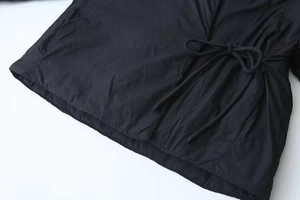 Detail view of black casual coat showing side drawstring tie and woven fabric texture