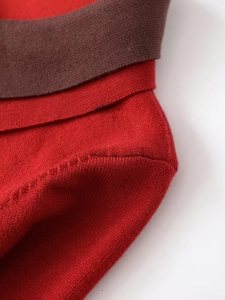 Detailed close-up of red knit sweater featuring brown ribbed edges and fine stitching