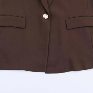 Close-up of brown blazer featuring a gold round button and symmetric flap pockets