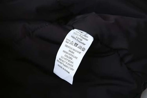 Detail of white wash care label on black winter coat showing 100% polyester material