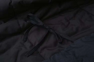 Detail of black quilted jacket featuring fabric texture and functional waist tie bow