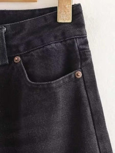 Detail of high waist black washed denim jeans with bronze rivets engraved with jeans text