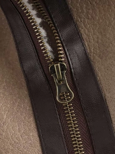 Detailed close-up of bronze metal zipper and textured brown leather on a short jacket