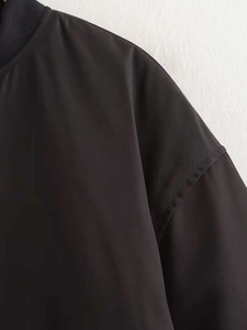 Detail of shoulder seam and ribbed collar on a black minimalist oversized bomber jacket